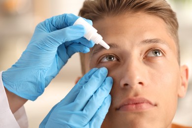 Photo of Doctor putting drops into man's eye indoors, closeup