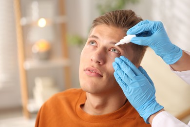 Photo of Doctor putting drops into man's eye indoors, closeup. Space for text