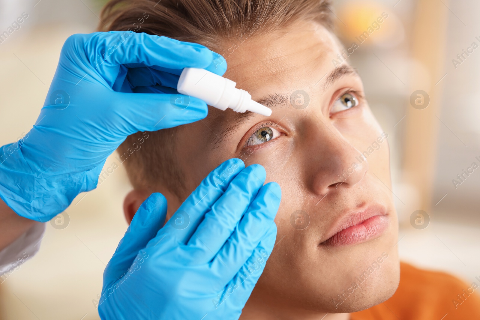Photo of Doctor putting drops into man's eye indoors, closeup