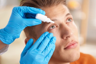 Photo of Doctor putting drops into man's eye indoors, closeup