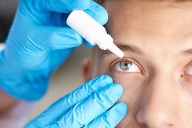Photo of Doctor putting drops into man's eye indoors, closeup