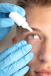 Photo of Doctor putting drops into man's eye indoors, closeup