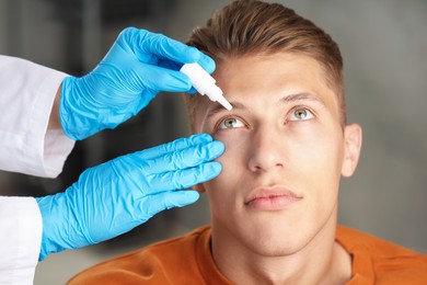 Photo of Doctor putting drops into man's eye indoors, closeup