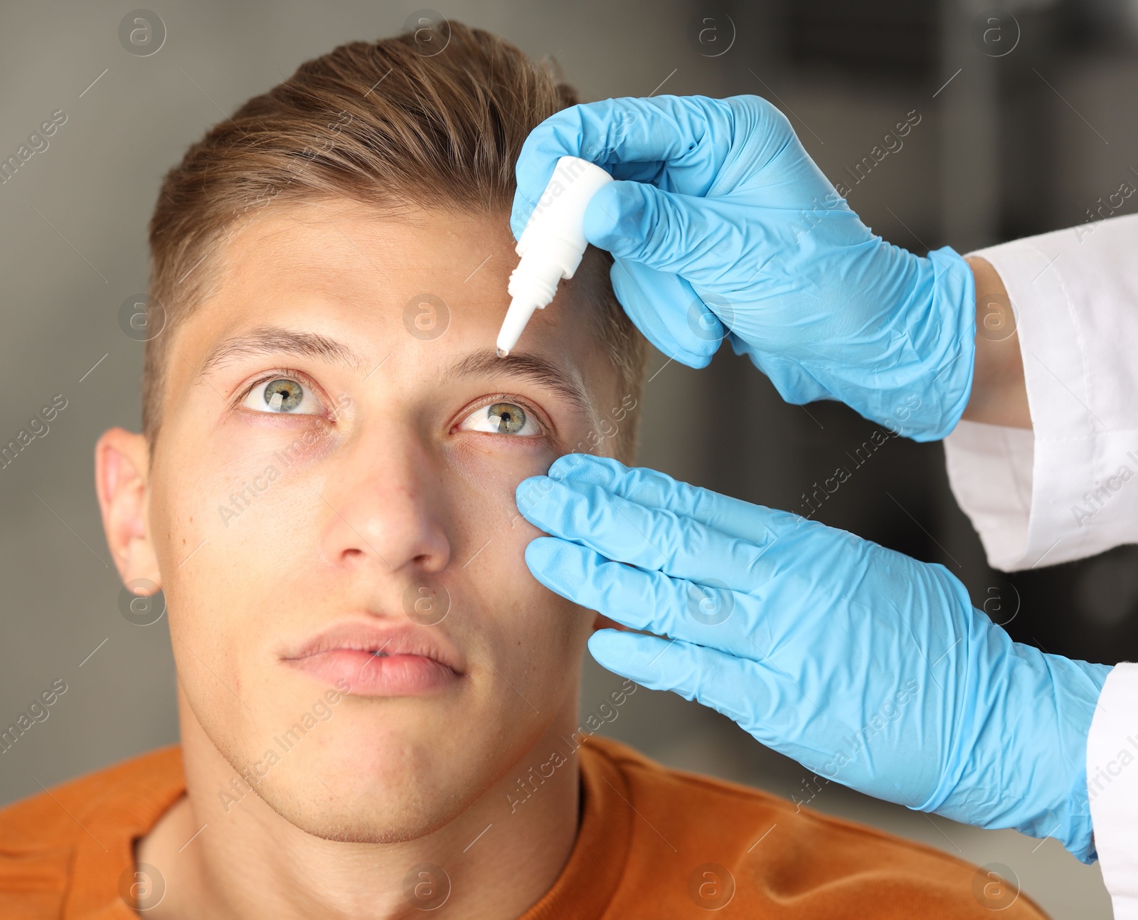 Photo of Doctor putting drops into man's eye indoors, closeup
