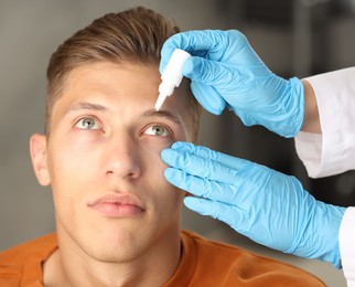 Photo of Doctor putting drops into man's eye indoors, closeup