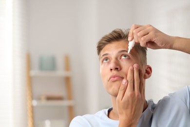 Photo of Young man applying eye drops at home. Space for text
