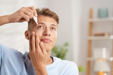 Photo of Young man applying eye drops at home. Space for text