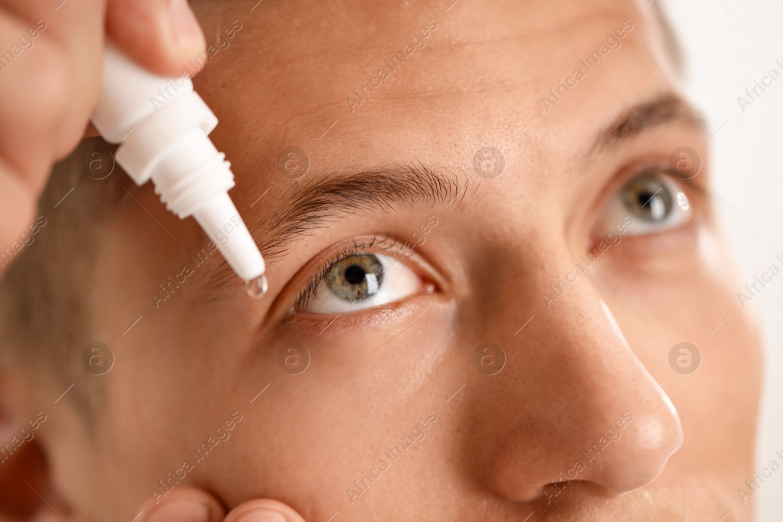 Photo of Man applying eye drops on light background, closeup