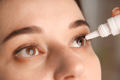 Photo of Woman applying eye drops on blurred background, closeup