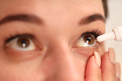 Photo of Woman applying eye drops on blurred background, closeup