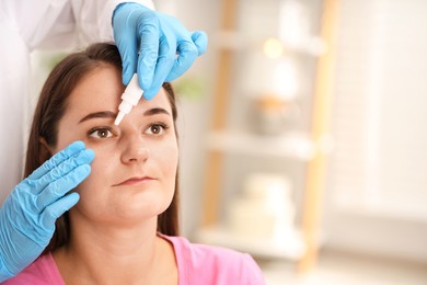 Photo of Doctor putting drops into woman's eye indoors, closeup. Space for text
