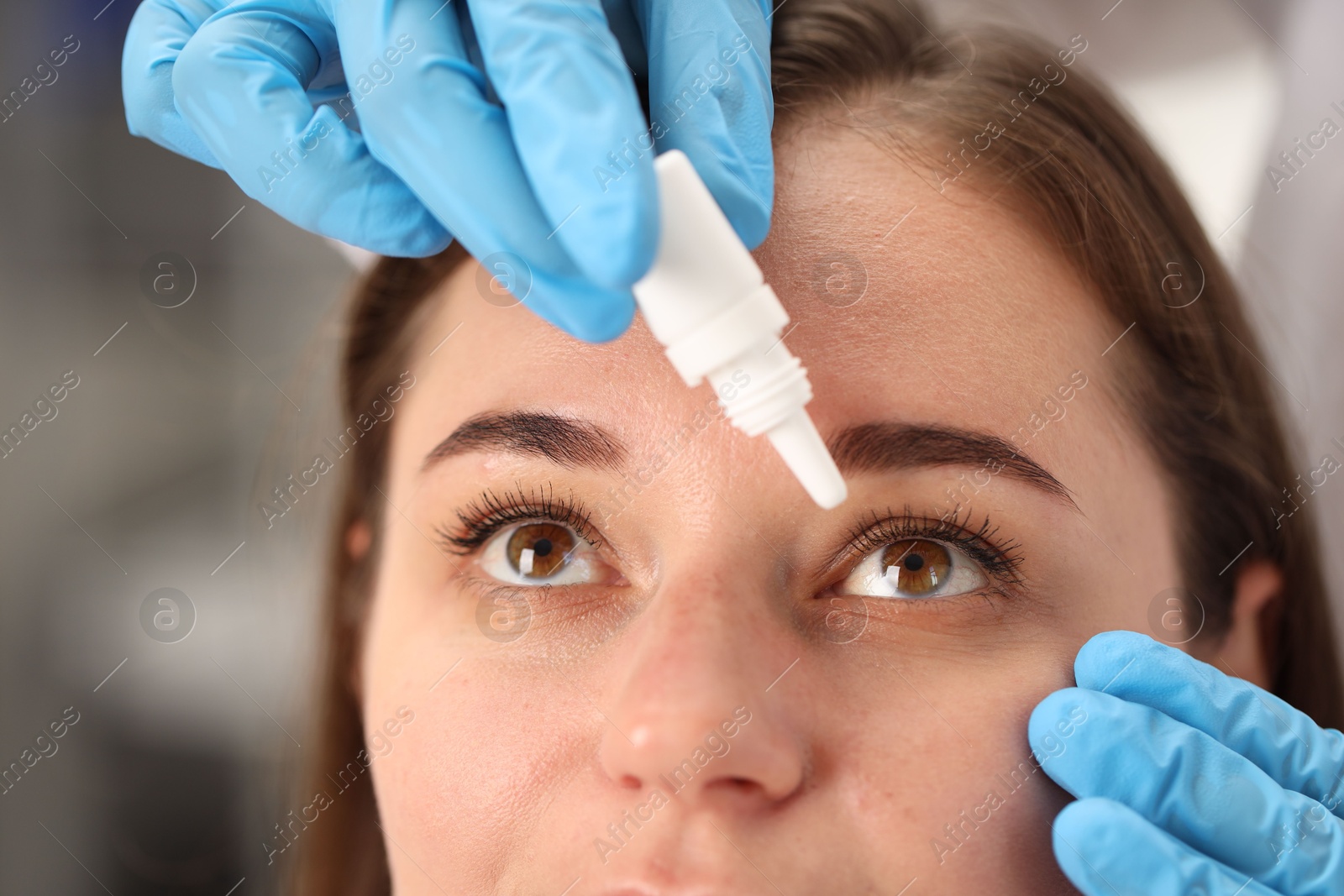 Photo of Doctor putting drops into woman's eye indoors, closeup