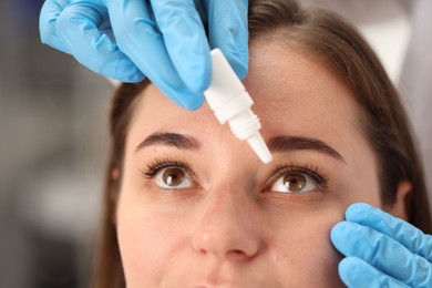 Photo of Doctor putting drops into woman's eye indoors, closeup