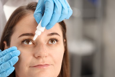 Photo of Doctor putting drops into woman's eye indoors, closeup. Space for text