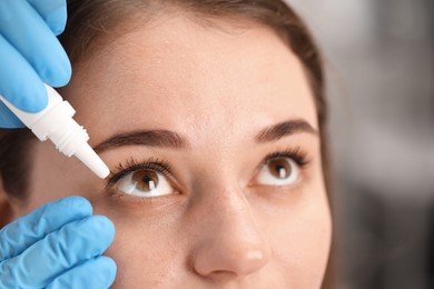 Photo of Doctor putting drops into woman's eye indoors, closeup