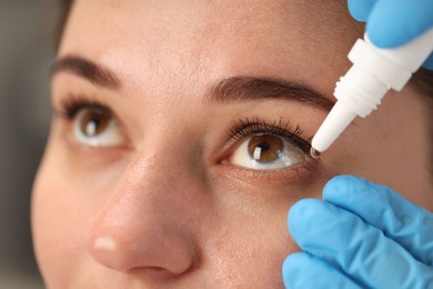 Photo of Doctor putting drops into woman's eye indoors, closeup