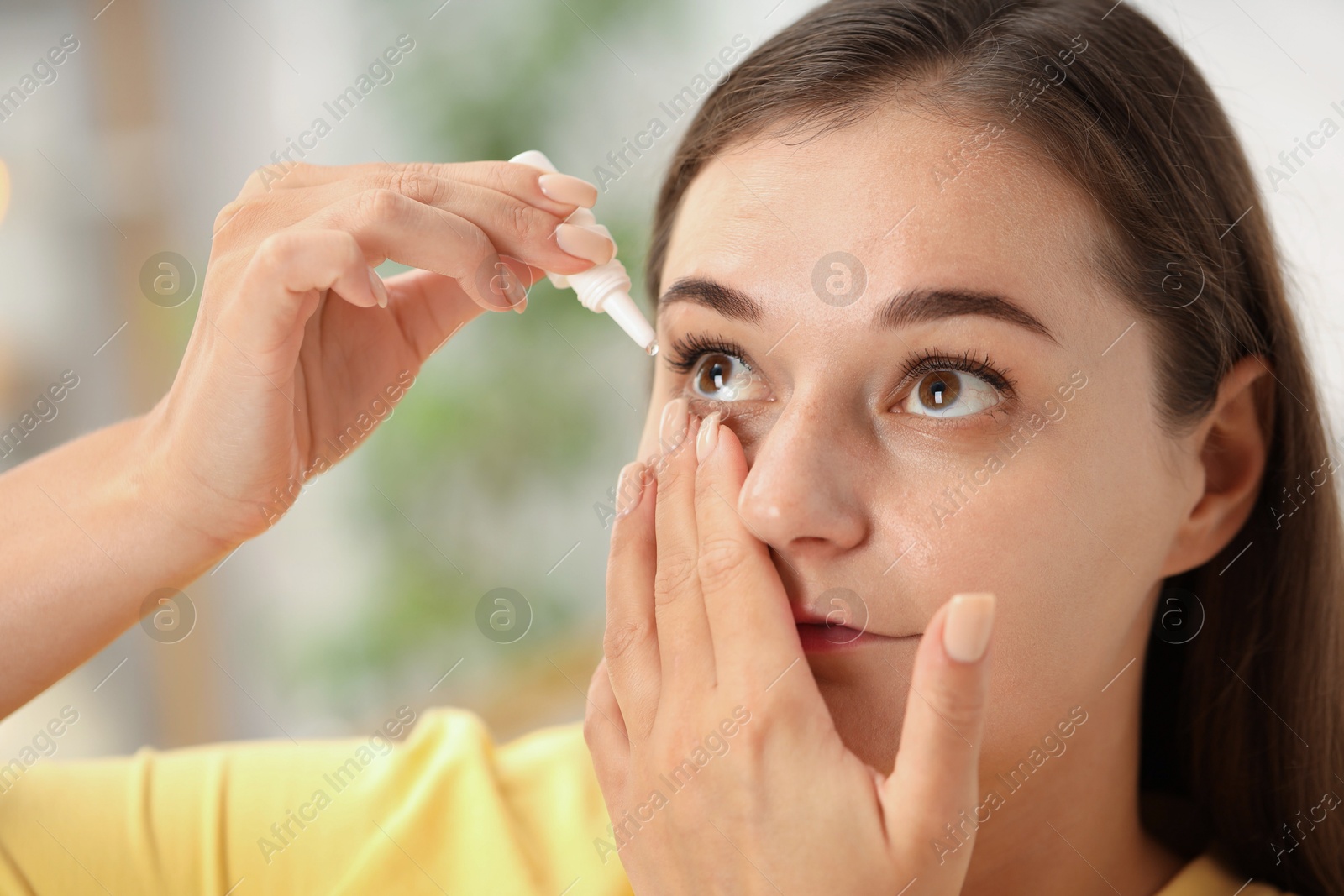 Photo of Young woman applying eye drops at home