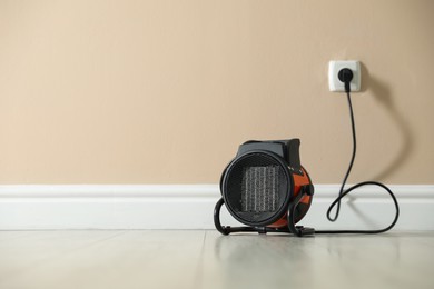 Photo of Electric fan heater on floor near beige wall indoors. Space for text
