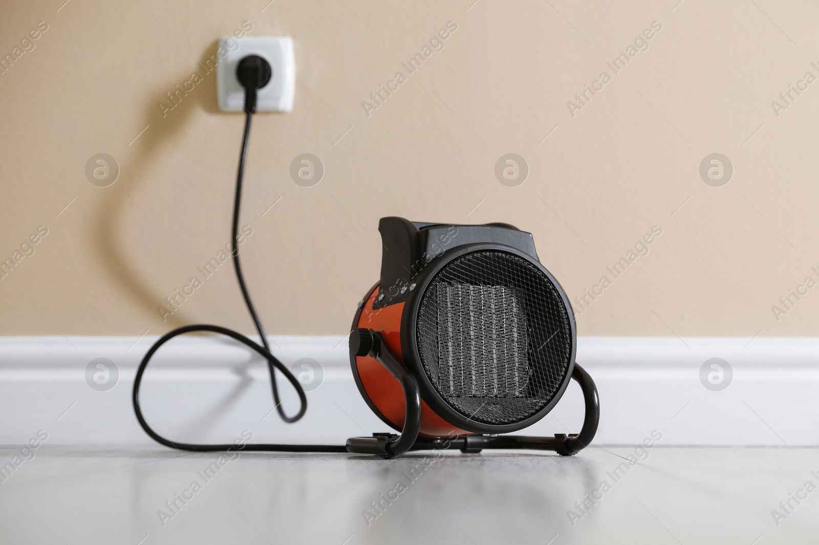 Photo of Electric fan heater on floor near beige wall indoors, closeup