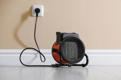 Photo of Electric fan heater on floor near beige wall indoors, closeup