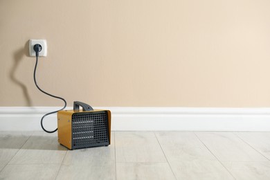 Photo of Electric fan heater on floor near beige wall indoors. Space for text
