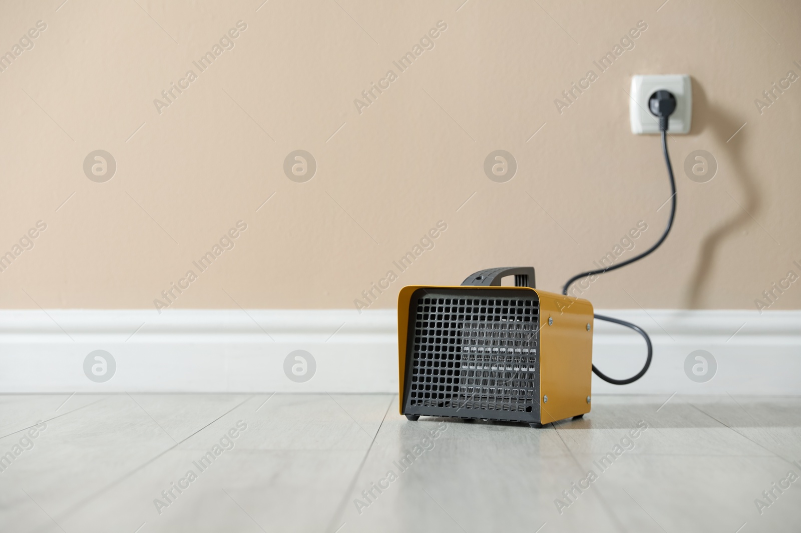 Photo of Electric fan heater on floor near beige wall indoors. Space for text