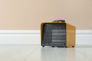Photo of Electric fan heater on floor near beige wall indoors. Space for text