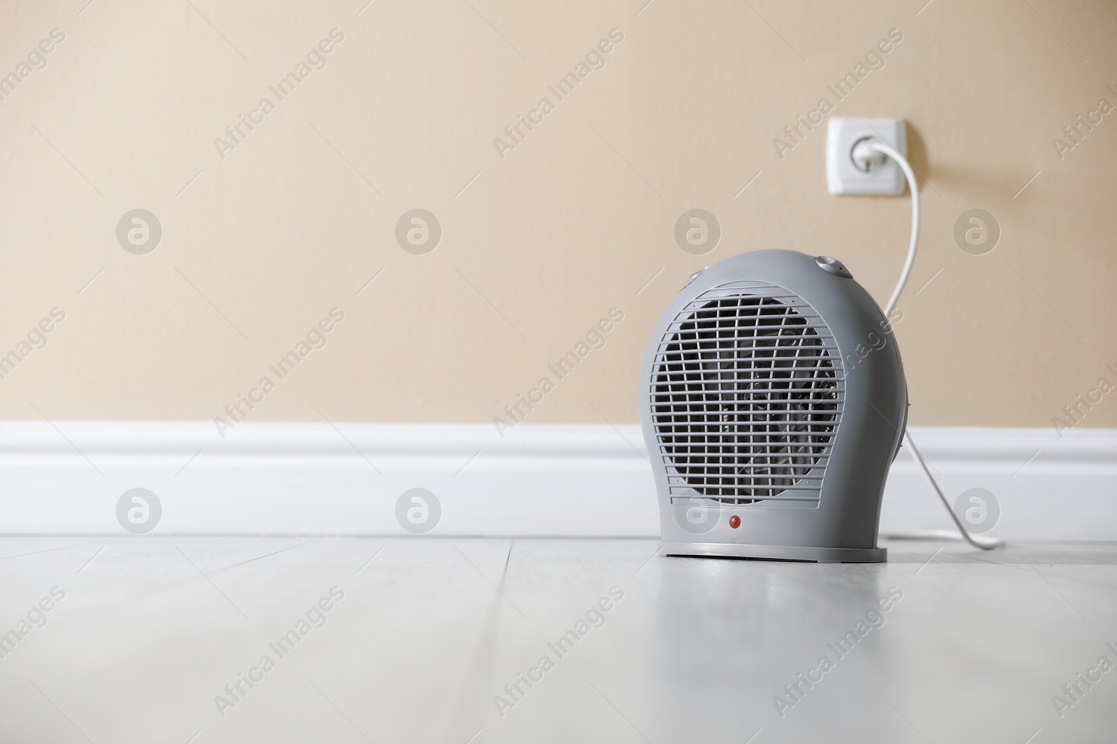 Photo of Electric fan heater on floor near beige wall indoors. Space for text