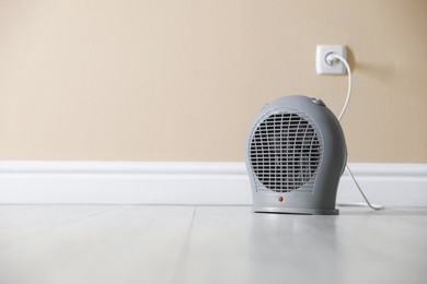 Photo of Electric fan heater on floor near beige wall indoors. Space for text