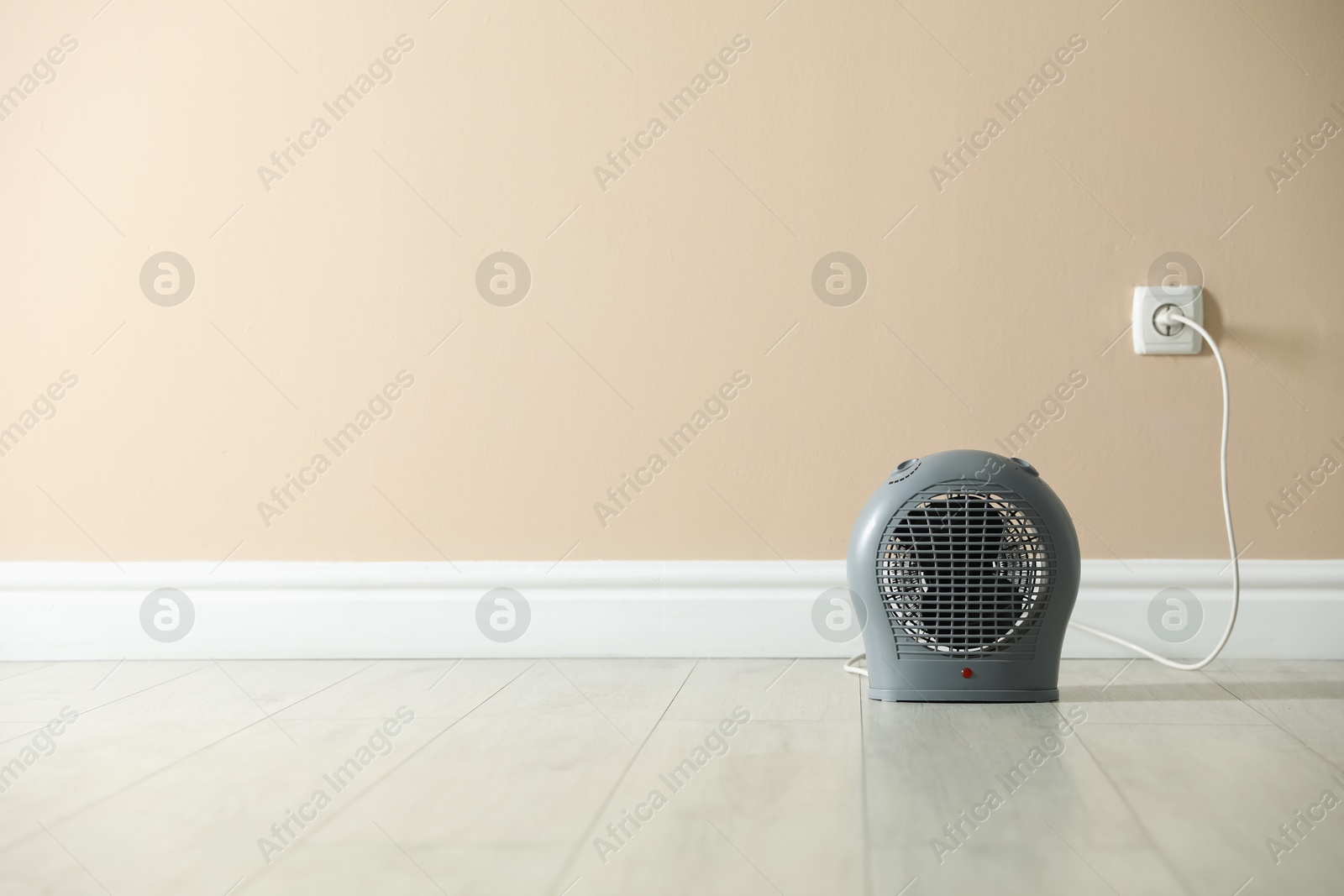 Photo of Electric fan heater on floor near beige wall indoors. Space for text