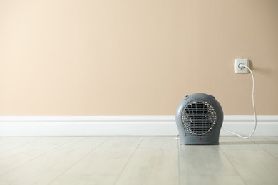Photo of Electric fan heater on floor near beige wall indoors. Space for text