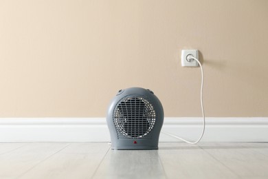 Photo of Electric fan heater on floor near beige wall indoors