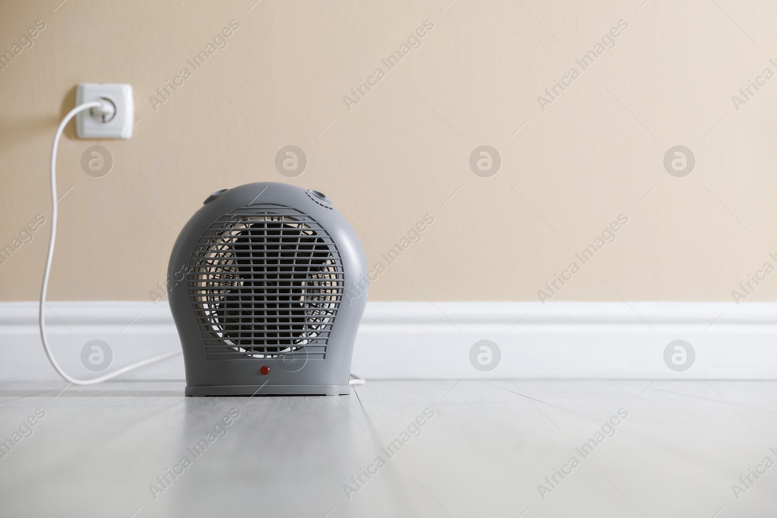 Photo of Electric fan heater on floor near beige wall indoors. Space for text