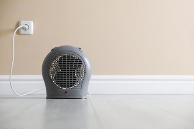 Photo of Electric fan heater on floor near beige wall indoors. Space for text