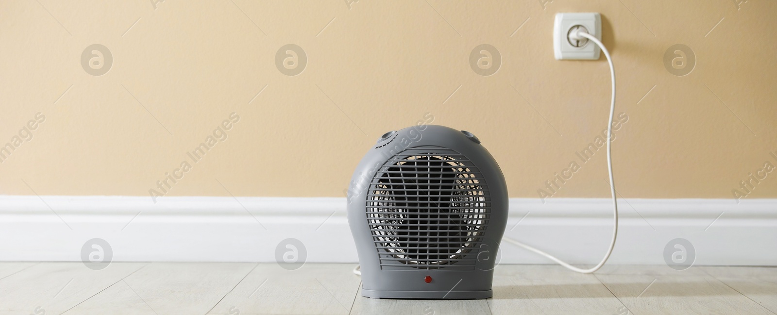 Photo of Electric fan heater on floor near beige wall indoors, closeup. Space for text
