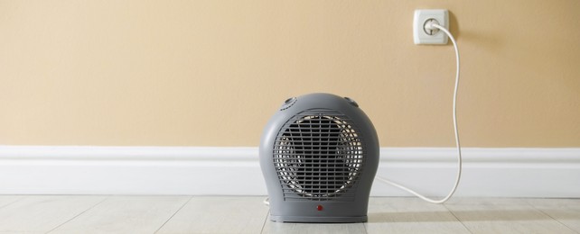 Photo of Electric fan heater on floor near beige wall indoors, closeup. Space for text