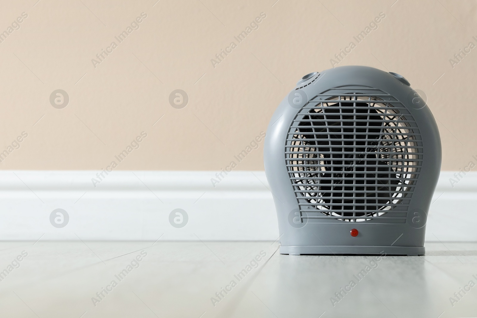Photo of Electric fan heater on floor near beige wall indoors, closeup. Space for text