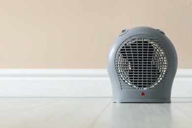 Photo of Electric fan heater on floor near beige wall indoors, closeup. Space for text