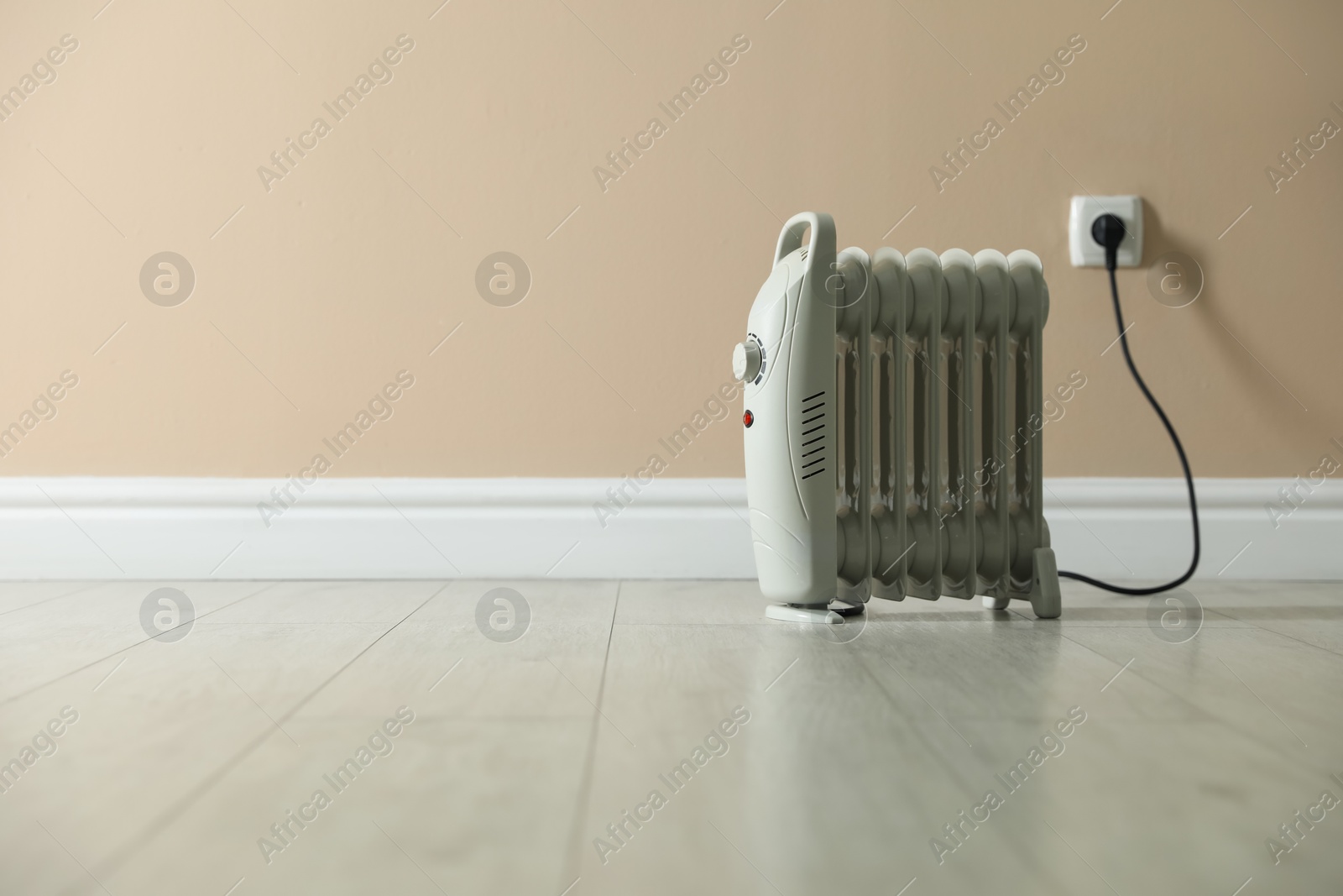 Photo of Electric heater on floor near beige wall indoors. Space for text