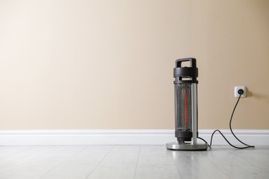 Photo of Electric heater on floor near beige wall indoors. Space for text