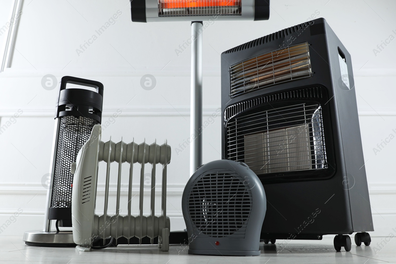 Photo of Different electric heaters on floor near light grey wall indoors, low angle view