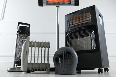Photo of Different electric heaters on floor near light grey wall indoors, low angle view