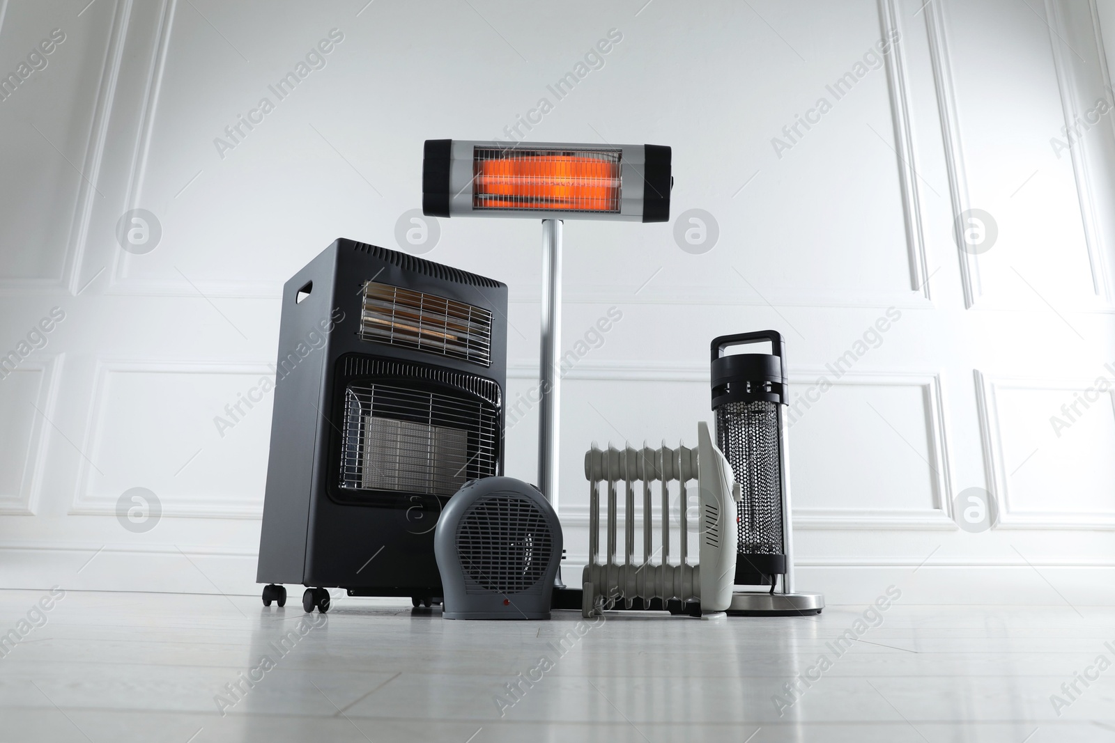 Photo of Different electric heaters on floor near light grey wall indoors, low angle view