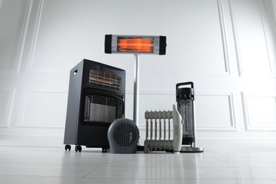 Photo of Different electric heaters on floor near light grey wall indoors, low angle view