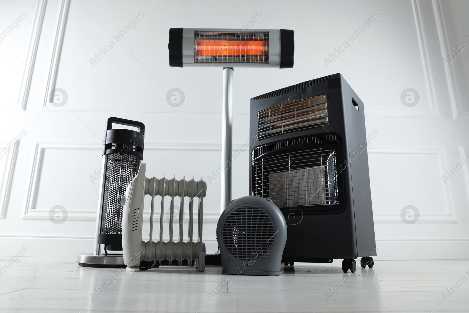 Photo of Different electric heaters on floor near light grey wall indoors, low angle view