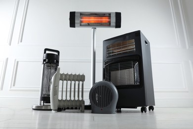 Photo of Different electric heaters on floor near light grey wall indoors, low angle view