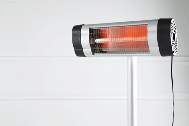 Photo of Electric infrared heater near white wall indoors, closeup. Space for text