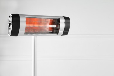 Photo of Electric infrared heater near white wall indoors, closeup. Space for text
