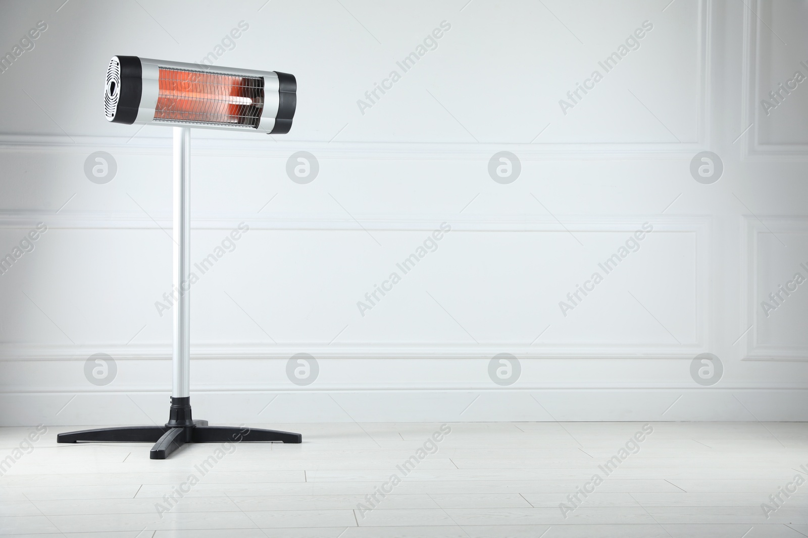 Photo of Electric infrared heater on floor near light grey wall indoors. Space for text