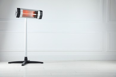 Photo of Electric infrared heater on floor near light grey wall indoors. Space for text